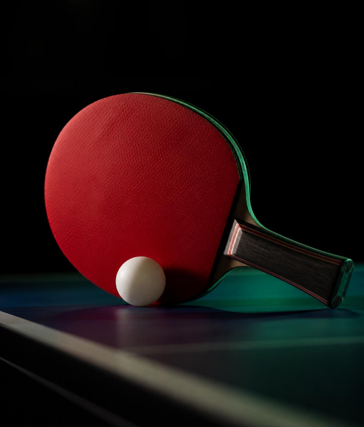Ping pong paddle and ball on a dark table
